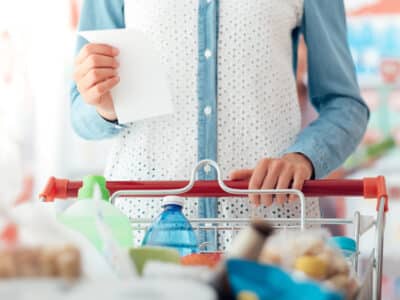 Woman doing grocery shopping at the supermarket, she is pushing a cart and checking a list