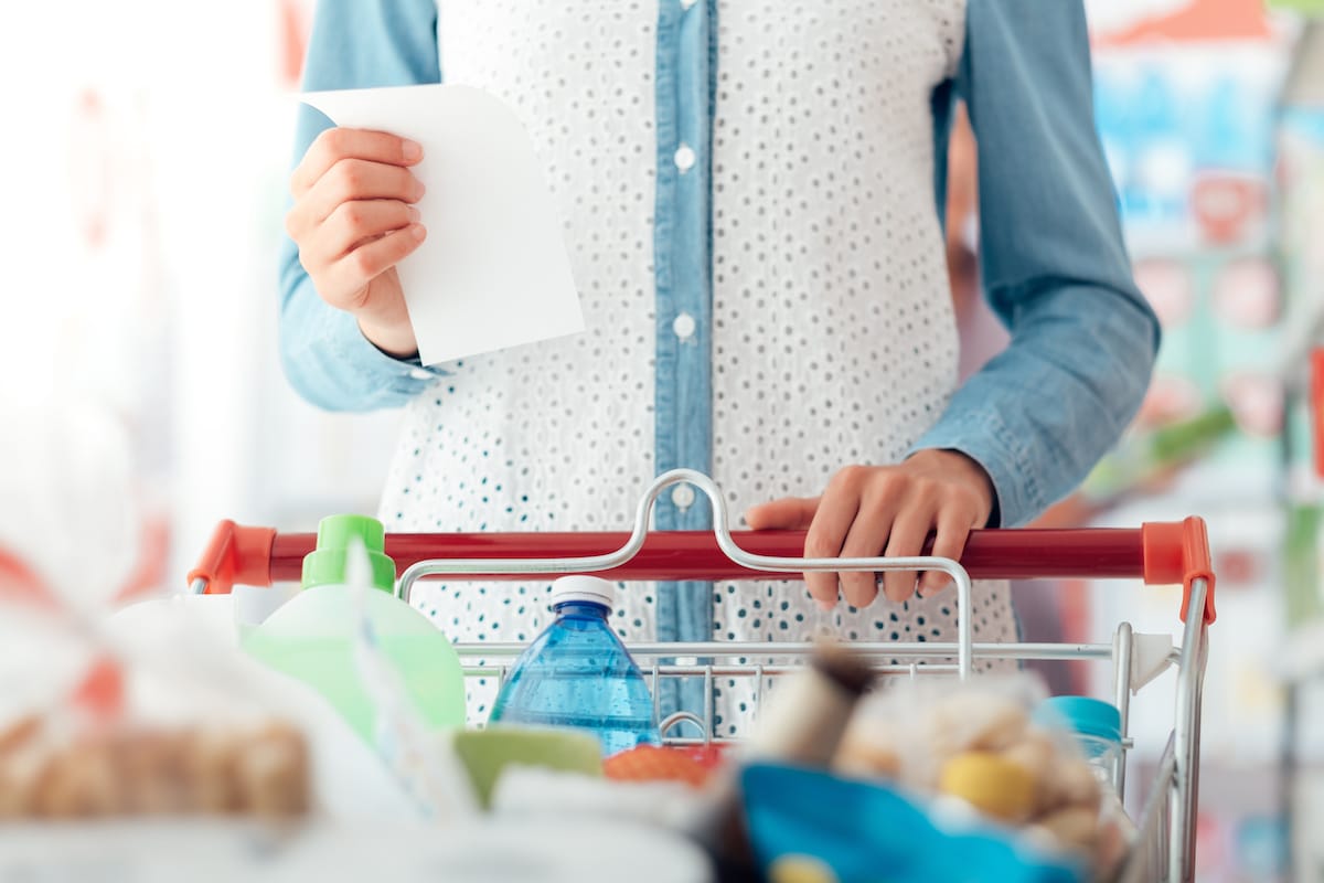 Woman doing grocery shopping at the supermarket, she is pushing a cart and checking a list