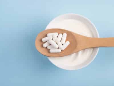 Capsules probiotic on a wooden spoon and bowl with homemade yogurt on light blue background.