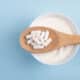 Capsules probiotic on a wooden spoon and bowl with homemade yogurt on light blue background.