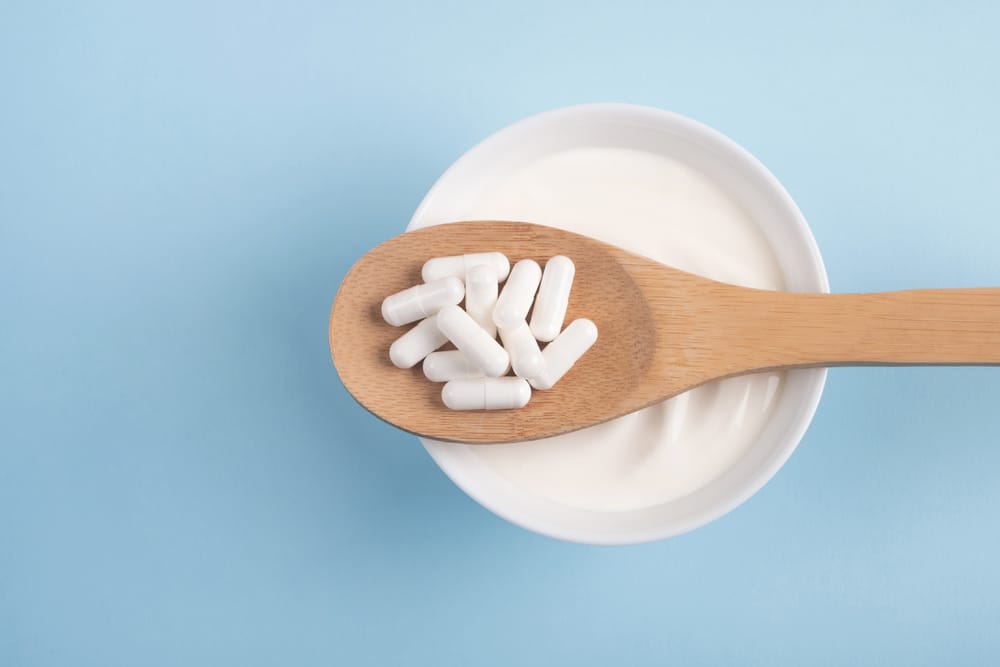 Capsules probiotic on a wooden spoon and bowl with homemade yogurt on light blue background.