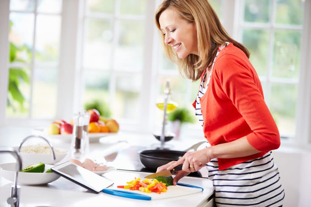 Woman cooking in kitchen, following recipe on tablet