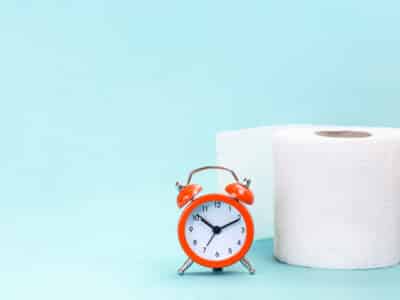 Alarm clock and toilet paper on blue background. Can antibiotics cause constipation?