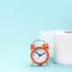 Alarm clock and toilet paper on blue background. Can antibiotics cause constipation?