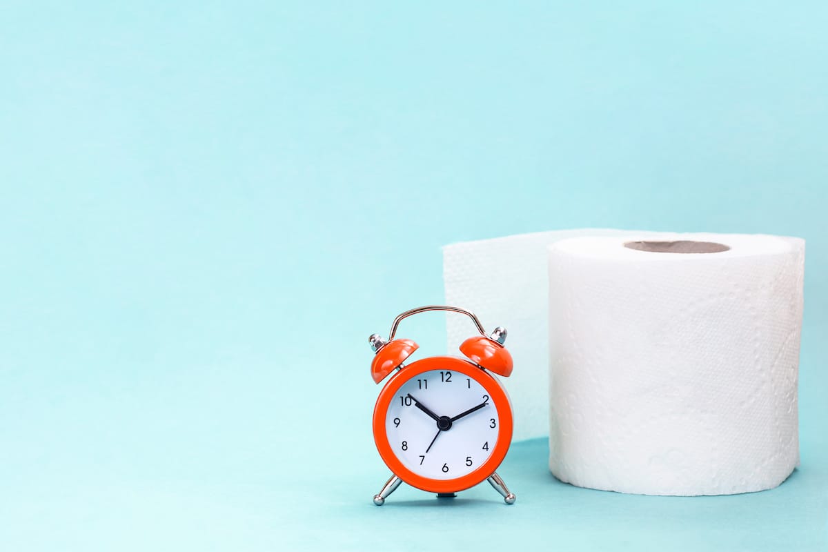 Alarm clock and toilet paper on blue background. Can antibiotics cause constipation?