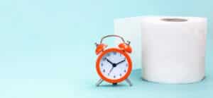 Alarm clock and toilet paper on blue background. Can antibiotics cause constipation?