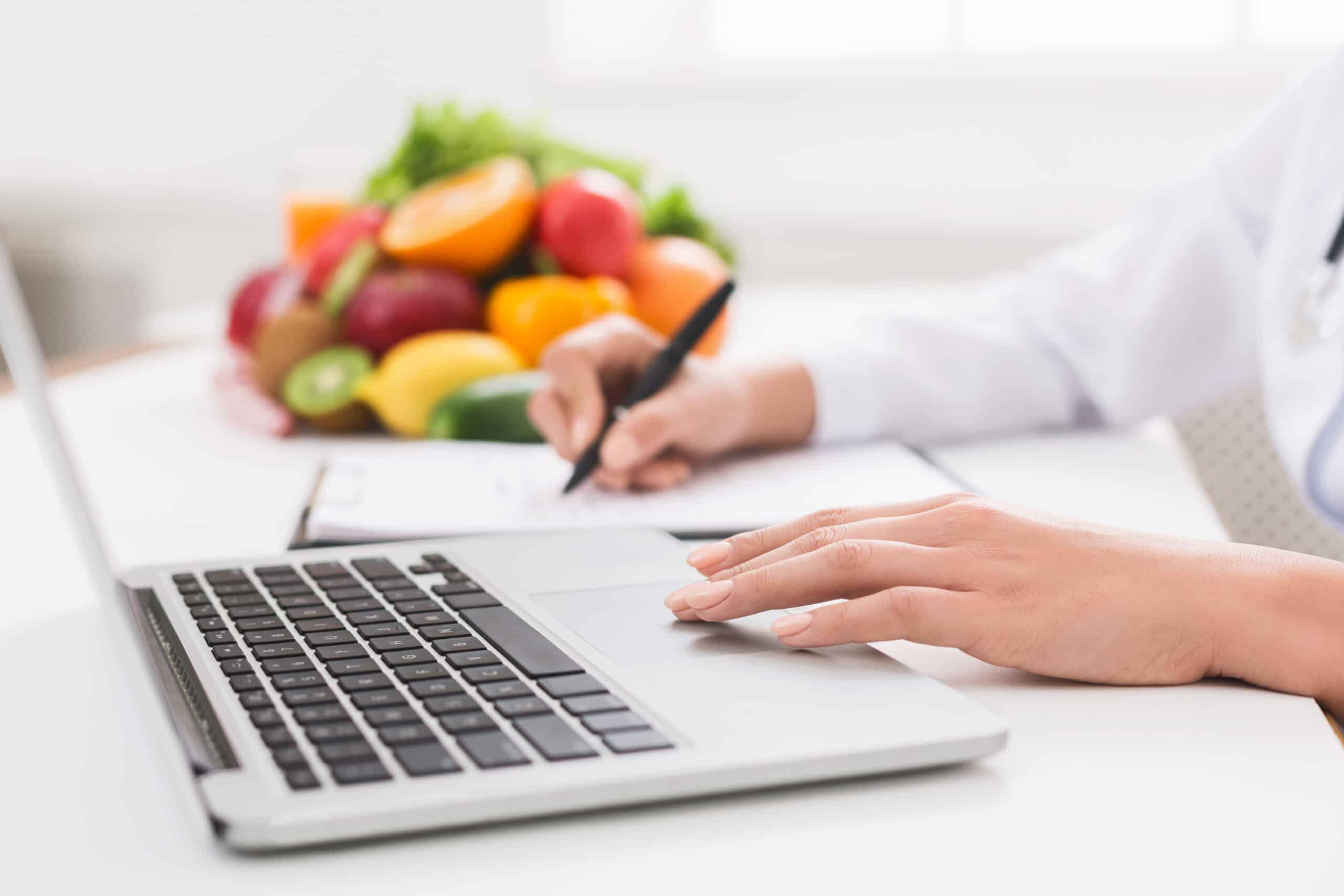 Woman using laptop with plate of healthy food in the background